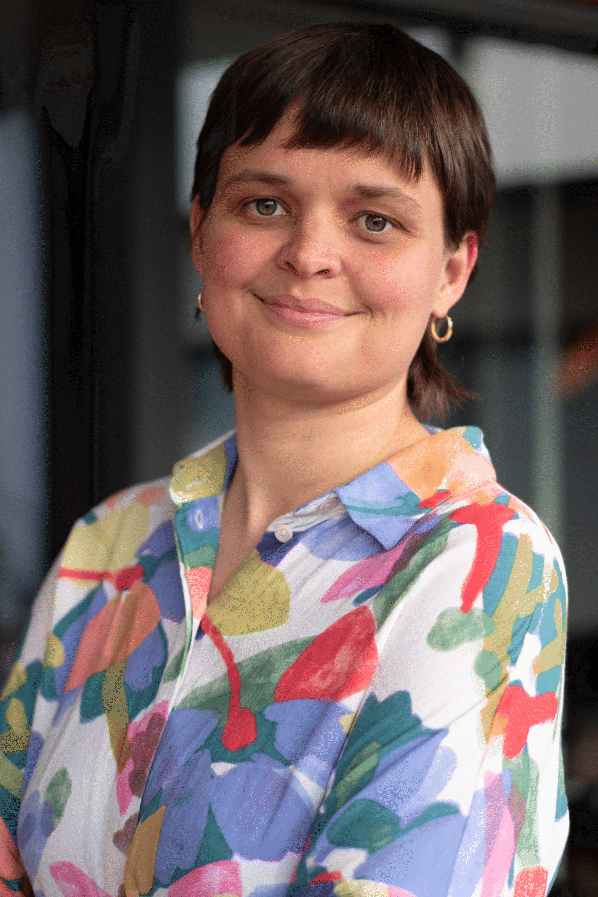 Eine lächelnde Person mit kurzem Haar und buntem Hemd.
