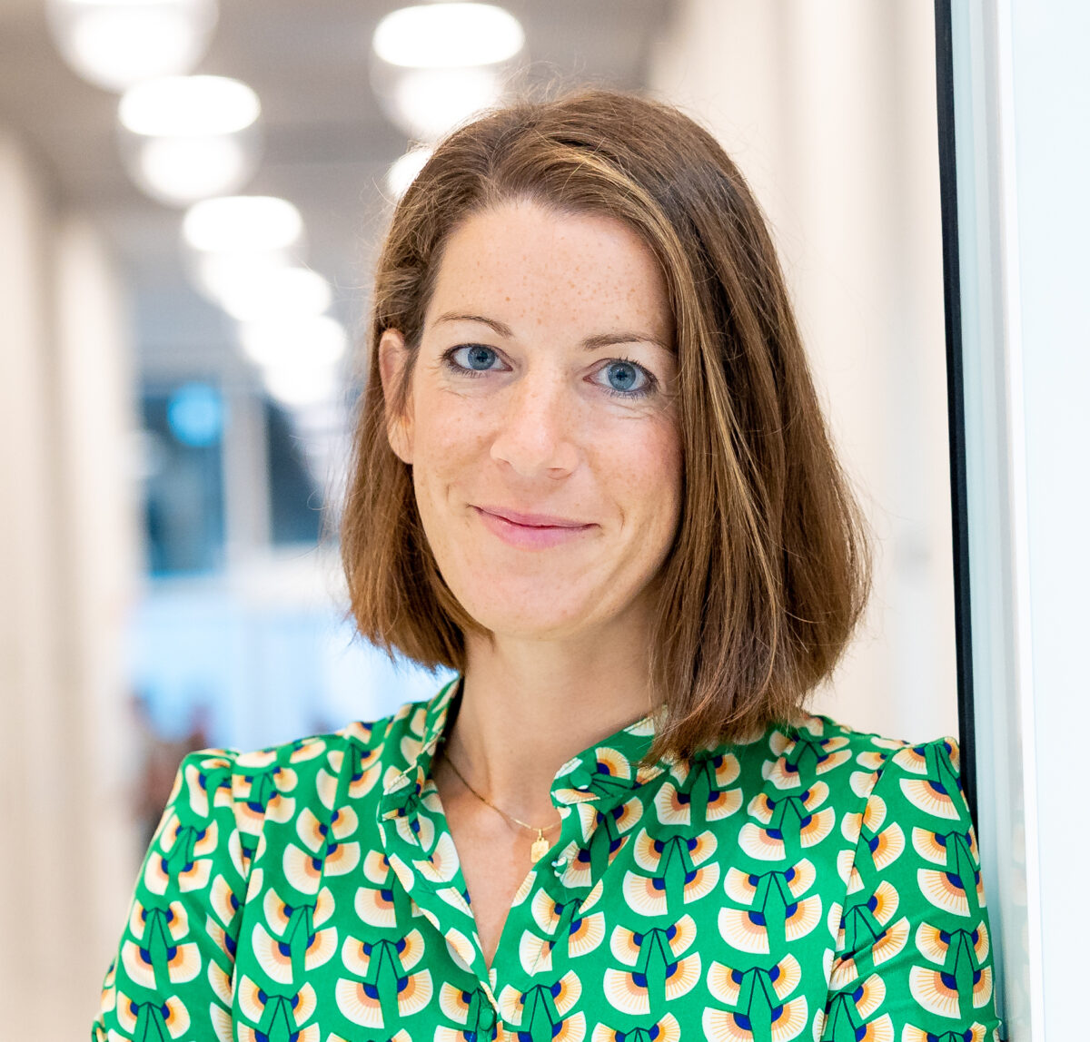 Eine Frau mit blonden Haaren trägt ein grünes Blumenhemd und lächelt.