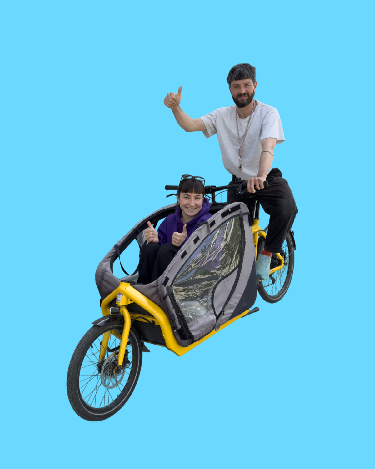 Zwei Personen fahren lachend auf einem gelben Lastenrad und zeigen Daumen hoch.